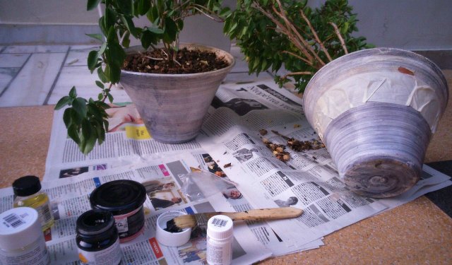 Two old gray planters being prepared with masking tape, paint and brushes for a makeover.