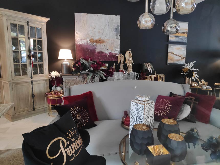 A warm living space with an off white sofa and a round glass coffee table exuding an eclectic vibe because of the deep burgundy decorations and the almost black wall in the background.