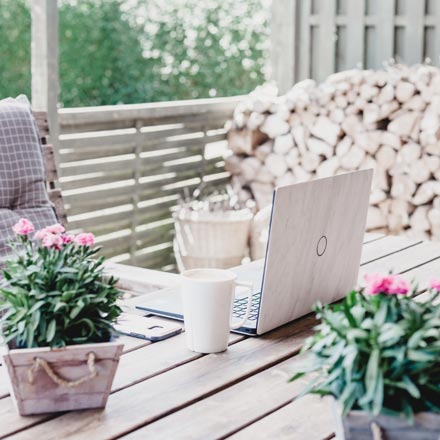A white laptop on a table outdoors with two planters next to it.