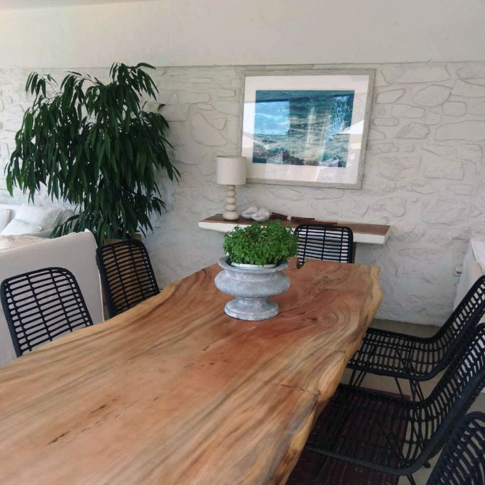 Home improvement ideas: View of a dining space with a large rustic wooden table, black rattan dining chairs and a white stone wall in the background. Greenery as splashes liven it all up.