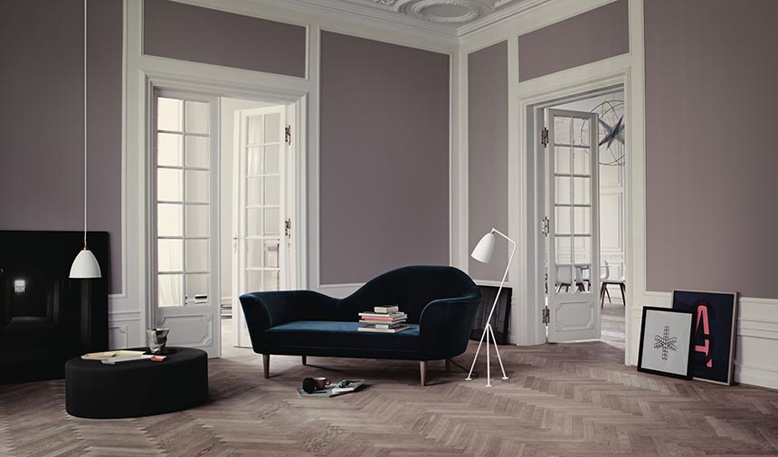 A velvet dark teal sofa in a muted mauve interior with a high ceiling and herringbone parquet flooring and a white Gubi floor lamp. Image by Nest.co.uk.