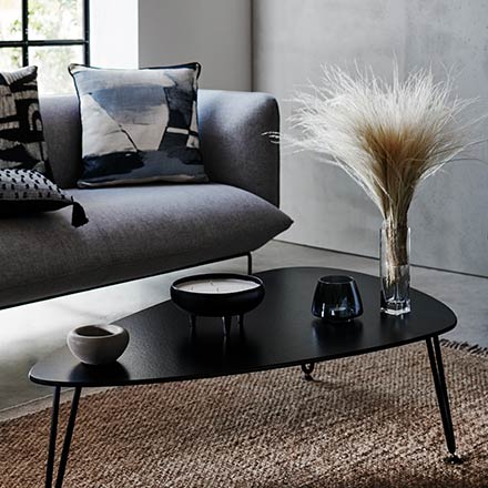 View of a vignette with a grey sofa, a black coffee table, and a large window in the background. Image via Sainsbury's Home.