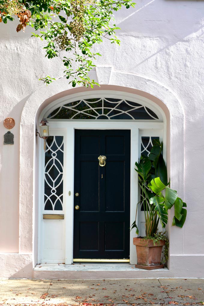 A black entrance door to an off white home with a planter.