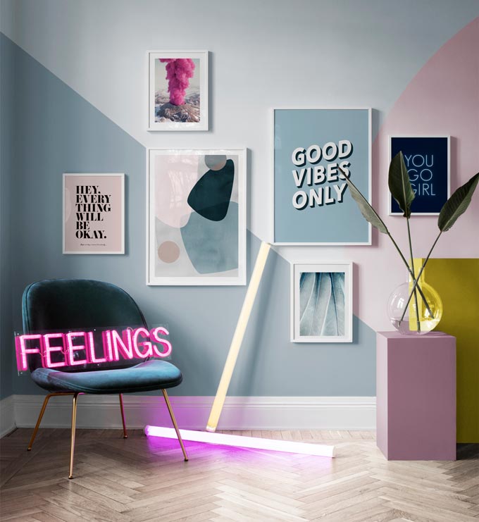 A vignette with a pop vibe to it, featuring a color blocked wall with an art gallery, a velvet upholstered armchair with a neon sign that reads feelings. Image by Desenio.
