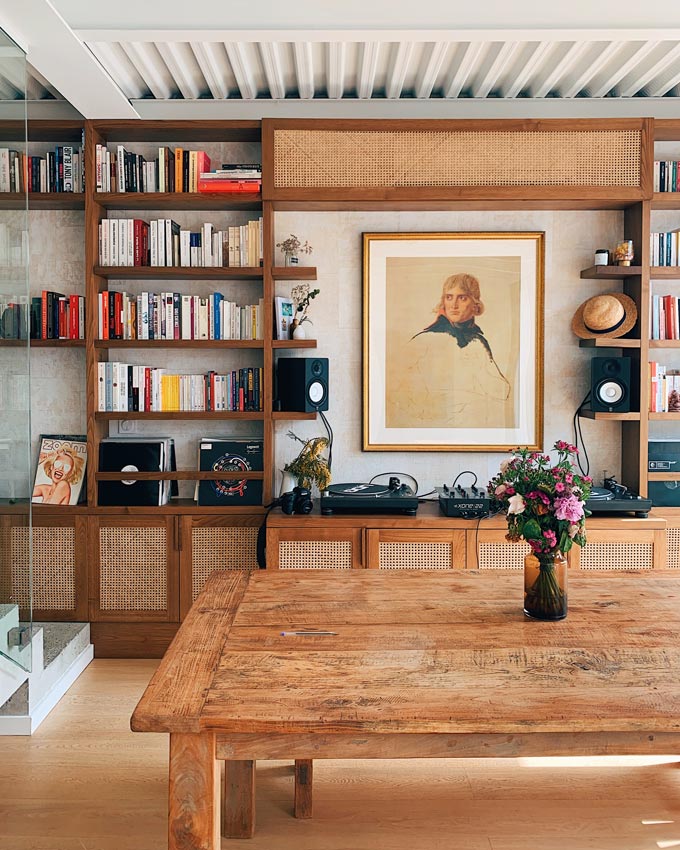 A room with a bookcase and a large wooden dining table.
