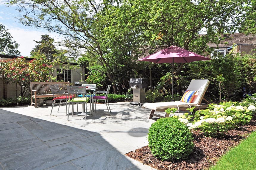 A beautiful backyard with a chaise longue, dining setup, sun umbrella during the daylight.