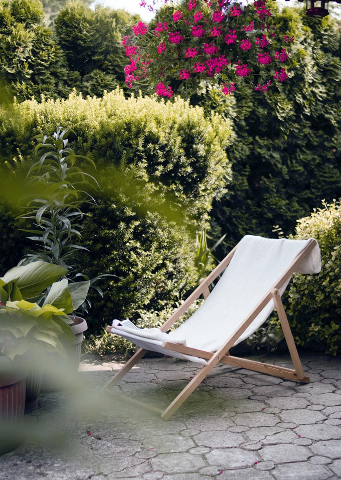 A sundeck chair on a paved patio surrounded with greenery.