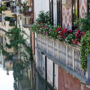 A closer view of a residential narrow balcony with planters that overlooks a canal in an Italian city