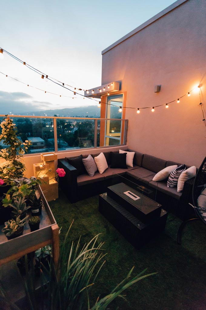 A private roof garden with a string of lights hanging over a sectional sofa.