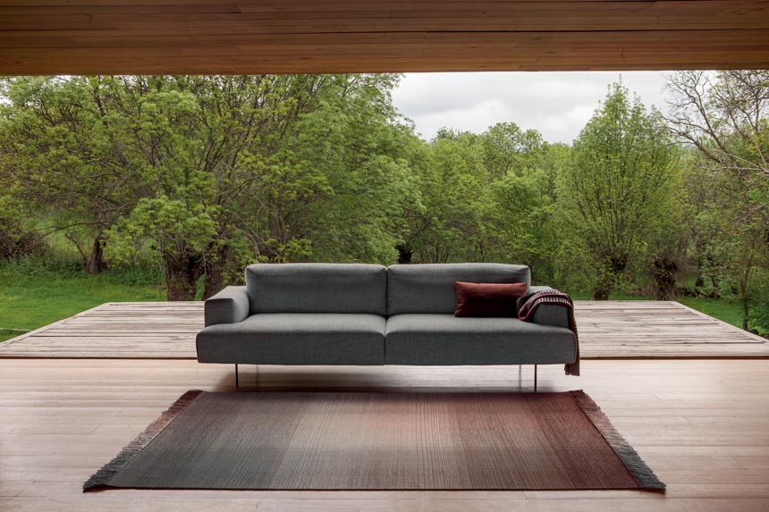 An ombre designer rug in front of a grey sofa. In the background a stunning garden view through an enormous window from floor to ceiling. Image via Nest.co.uk.