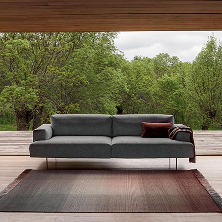 An ombre designer rug in front of a grey sofa. In the background a stunning garden view through an enormous window from floor to ceiling. Image via Nest.co.uk.