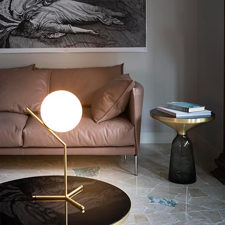 View of a vignette with a leather sofa, a glass side table and the IC T1 high table lamp designed by Michael Anastassiades on a glass coffee table. Image via Nest.co.uk.