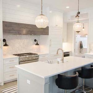 A stylish white kitchen with a large white island and chandelier pendant lights over it.