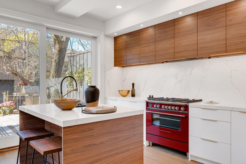 A contemporary kitchen with an island, lots of wooden detail and a deep red stove.