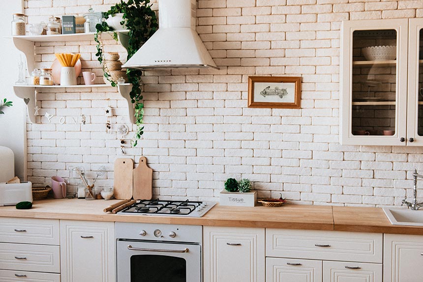 A farmhouse style kitchen with a wooden countertop and off white brick wall accent as a backsplash.