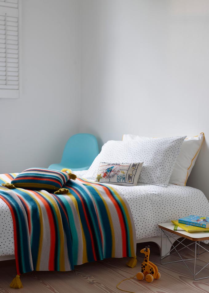 A nicely made kids bed with a striped colorful throw on it. Image by Christy.