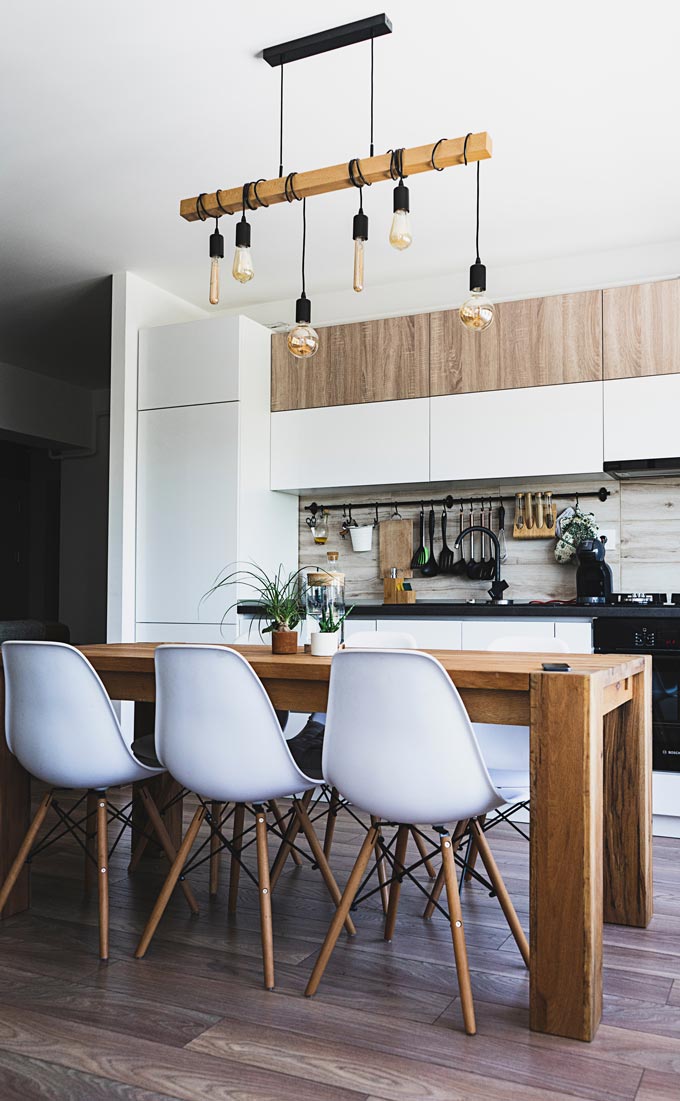 A contemporary kitchen with white cabinetry and a large wooden dining table in the foreground. Is a kitchen island a good kitchen improvement idea?