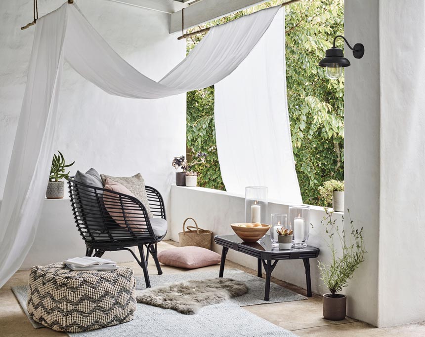 What a dreamy outdoor setup with a black rattan chair, a chevron pattern pouf, and an airy canopy. Image via John Lewis.