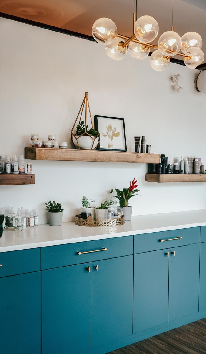 A teal blue kitchen with rustic floating shelves atop the cabinetry looking super stylish.