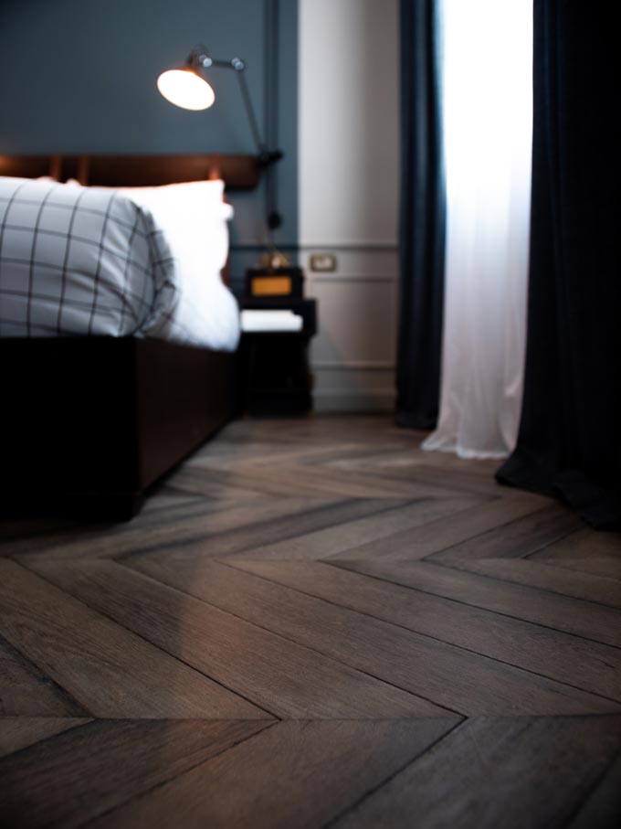 A bedroom with a blue accent wall in the background and dark chevron pattern hardwood flooring.