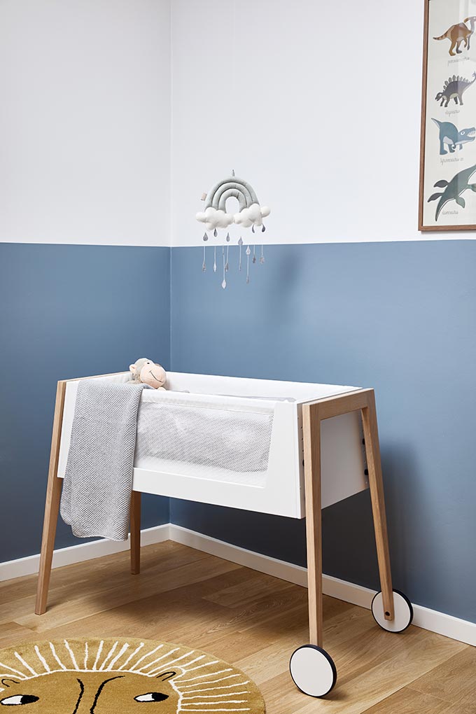 A cot bed in a baby nursery room with color blocked blue walls. Image by Cuckooland.