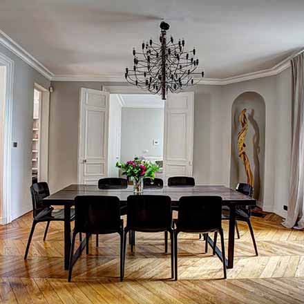 A stylish interior with a black dining table and chairs, black chandelier with a chevron pattern hardwood floor
