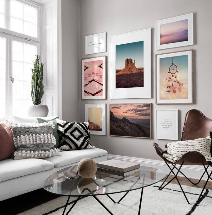 A contemporary bright living room with a white sofa and glass top round coffee table, featuring a gallery wall. Image by Desenio.