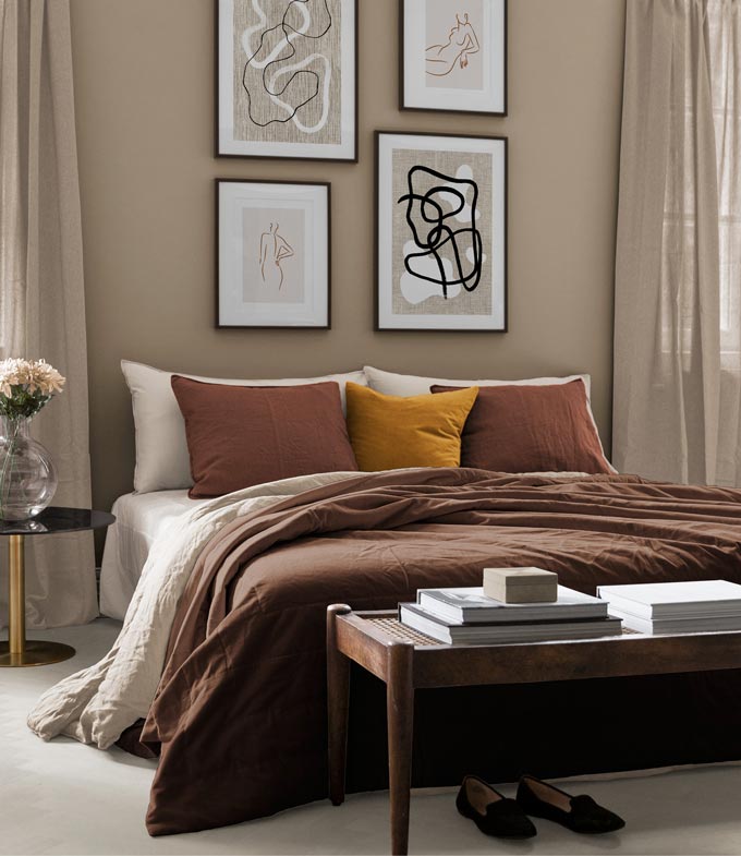 A contemporary bedroom in a rusty tone palette with a four print art gallery featuring over the bed. Image via Desenio.