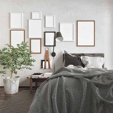 messy modern bedroom with an unmade bed and a series of blank picture frames on the wall lit by daylight from a large window with curtains