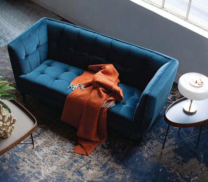 A blue velvet sofa with a side table next to it and a rusty hue throw on it. Image by Harvey Norman.