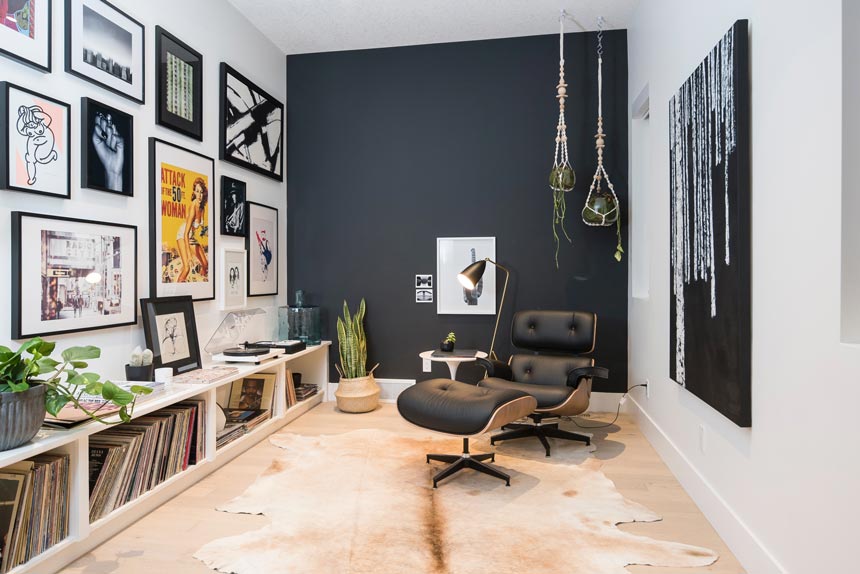 A contemporary setting with an Eames lounge chair, a dark grey accent wall in the background and a art gallery wall.