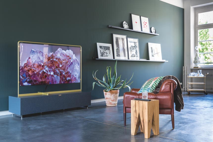 A deep saturated green wall makes the perfect backdrop for these picture ledges next to a TV frame. The big plant and the side table next to the leather armchair look so good together.