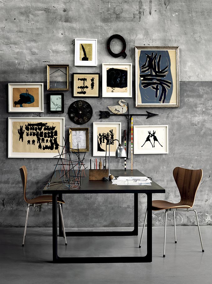 An art gallery wall on a grey cement wall with a table and chairs under it. Image by Nest.