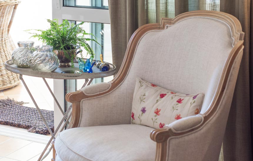 A vignette by a window door, with a vintage armchair, a side table and decor adding pops of color in this neutral palette scheme.