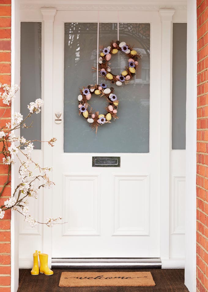 A white front door decorated with two wreaths for Easter celebrations. Image via John Lewis.