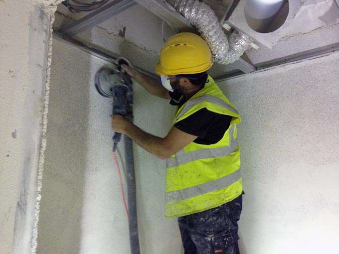 A handyman sanding down newly installed terrazzo on a wall.