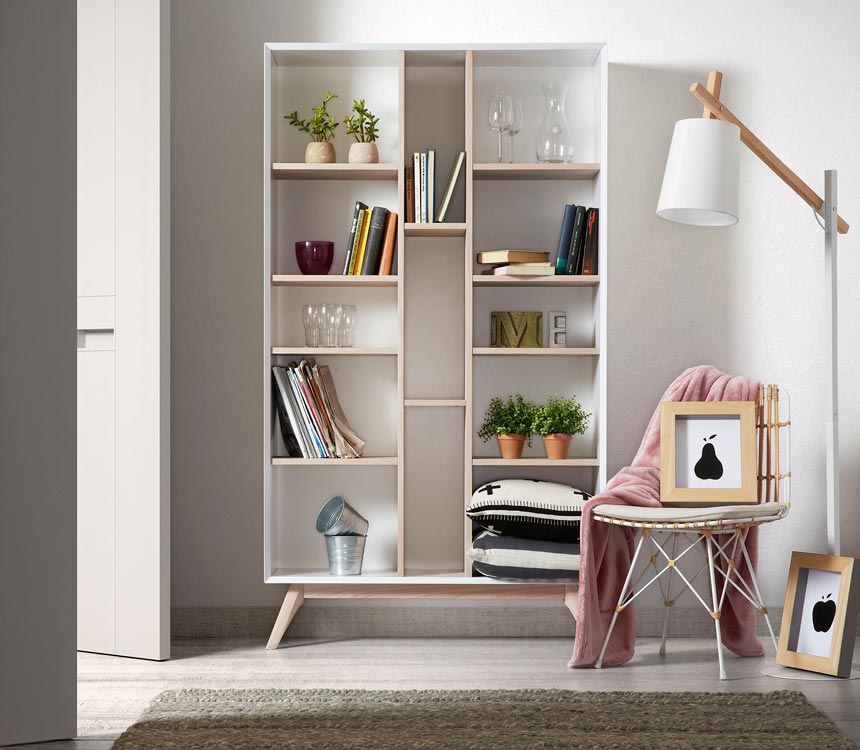 A white bookcase with decor and some books style with some greenery too next to a white chair and floor lamp. Image by Cuckooland.