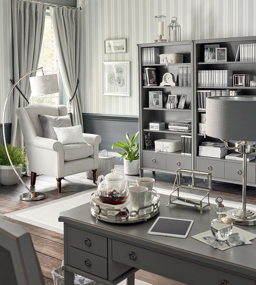 A home office with bookcase units, a white armchair, a grey French style desk and a very grey color palette governing everything. Image by Laura Ashley.