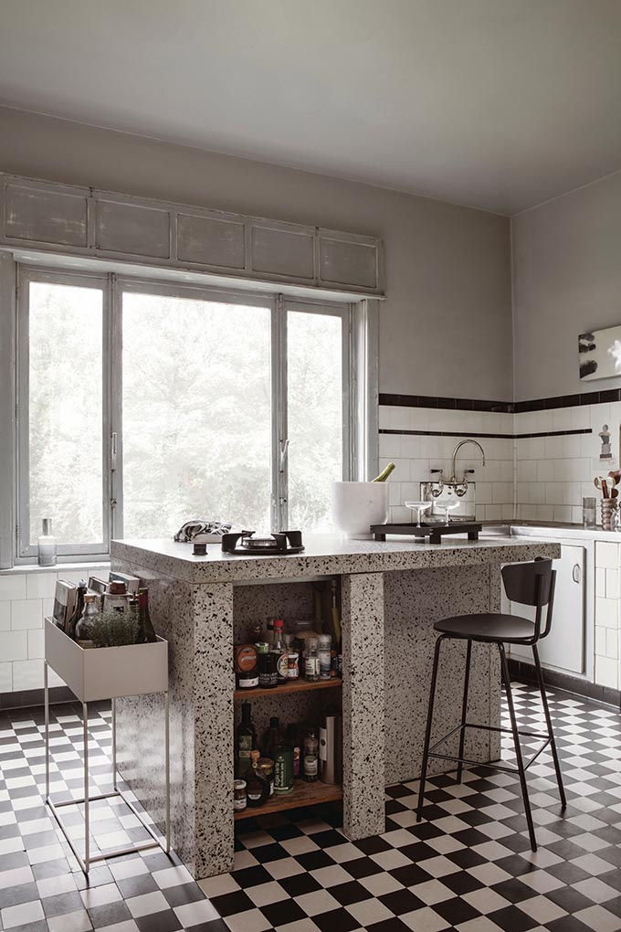 A kitchen with a tiled black and white patterned floor and a terrazzo island. Next to stands the Ferm living planter box. Image by Nest.