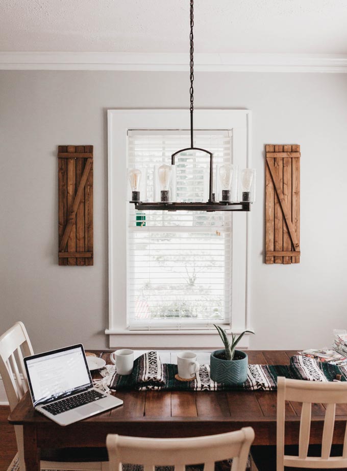 A dining space with a framed white window that has white Venetian blinds.