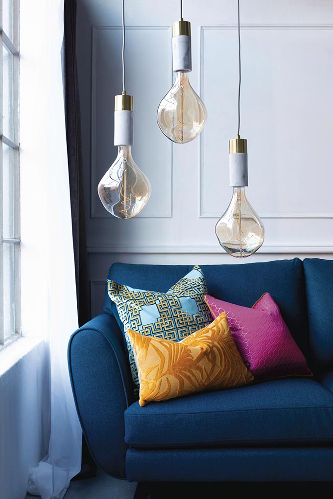 A blue sofa besides a window with three pendant lights hanging over that sofa's end.