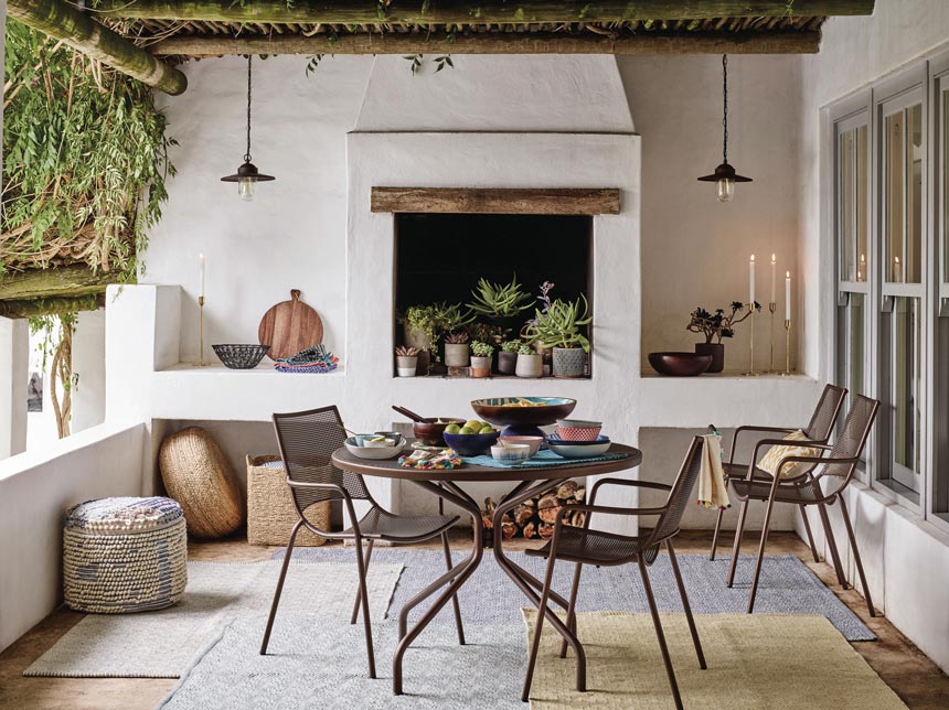 Basics lighting design: A beautiful outdoor setup under a pergola with lights hanging from either side of the fireplace that's filled with planters. Image by John Lewis.