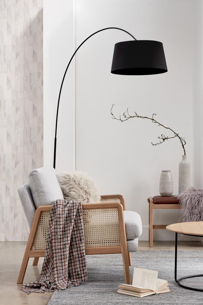 A floor lamp with a black shade adds definition in this vignette with a cane armchair and decorated side bench. Image by John Lewis.