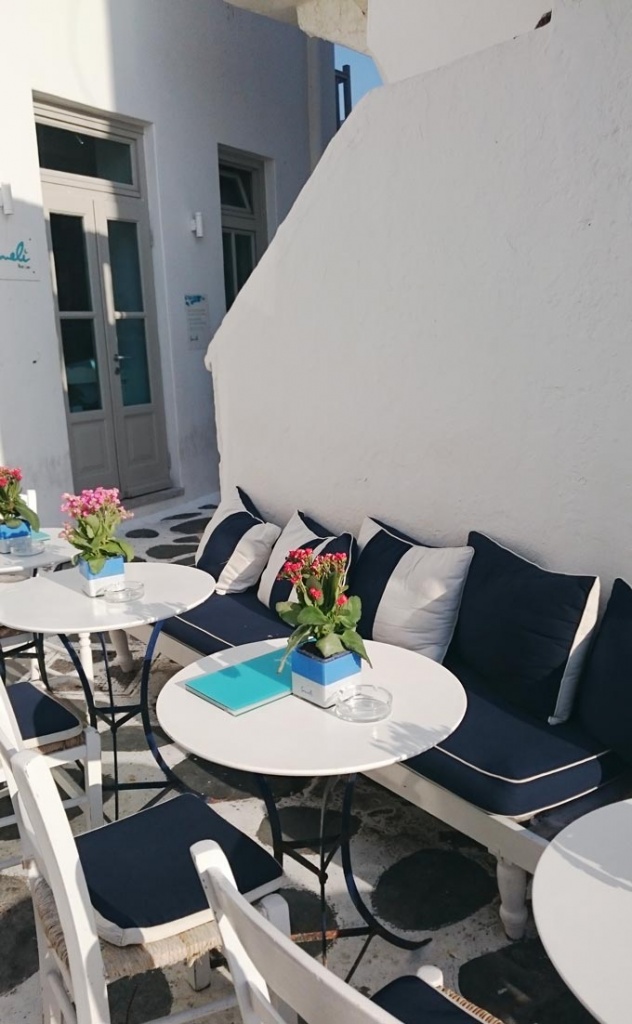 An outdoor setting with a sofa bench and navy blue pillows and round dining tables in an alley in Mykonos.