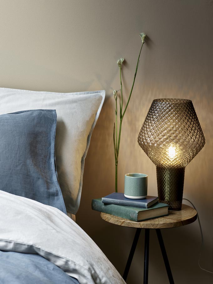 Close up of a bedroom vignette with a marble top side table as a nightstand by a bed. Image by Debenhams.