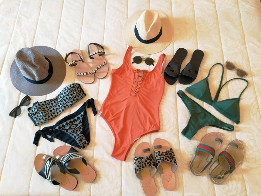 A flatlay with swimsuits, hats and flat sandals all suitable of packing to the Greek islands.