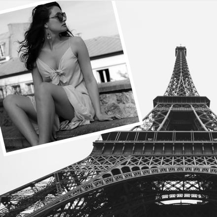 A black and white image of a young beautiful woman sitting somewhere outdoors wearing a summer dress. In the background image of the Eiffel Tower