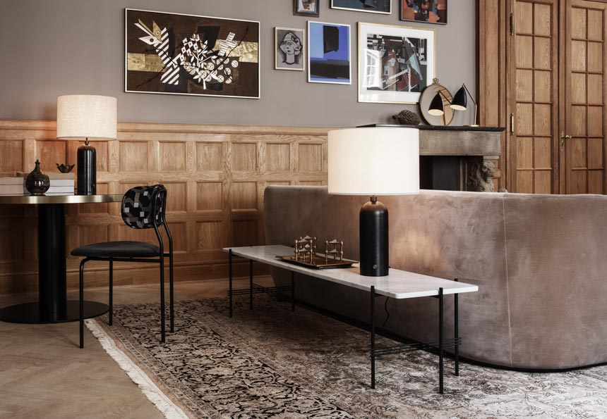 A super stylish living room with an art gallery wall on a taupe hue wall, a muted beige curved velvet sofa and behind a marble table top on a black steel frame. Image by Nest.