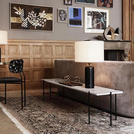 A super stylish living room with an art gallery wall on a taupe hue wall, a muted beige curved velvet sofa and behind a marble table top on a black steel frame. Image by Nest.