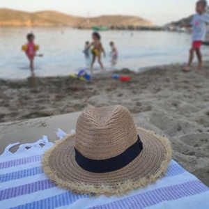 A straw hat on a beach towel by a sandy beach with children playing in the water in the background. Image by Velvet.